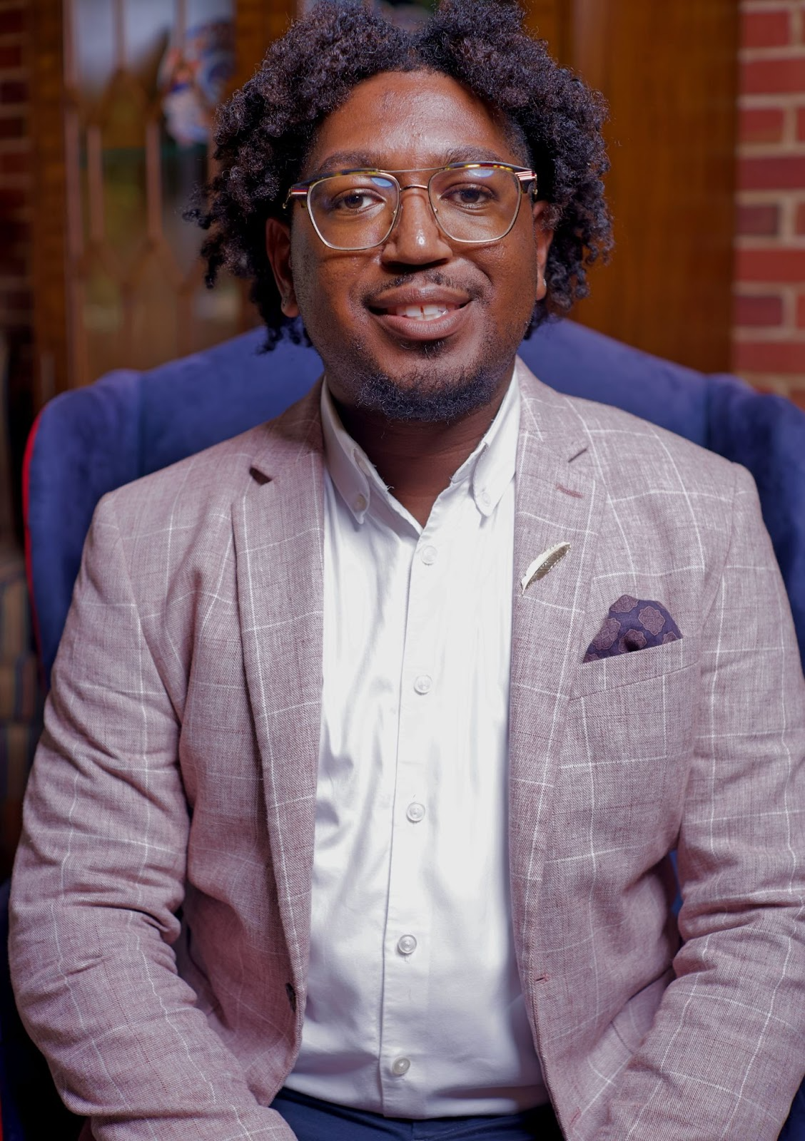Brian Wesley Harrington appears in a lavendar suit with a purple pocket square and white collared shirt. He is wearing glasses.
