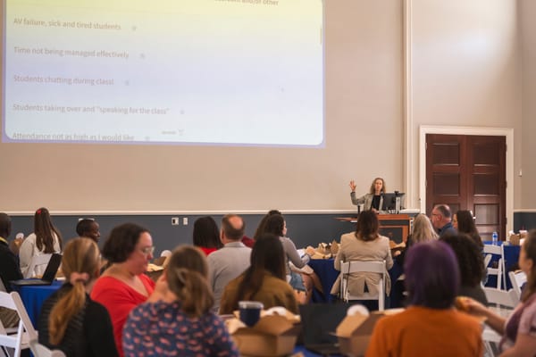 A group of people sitting at round tables eating lunch listen to speaker Jessamyn Neuhaus.
